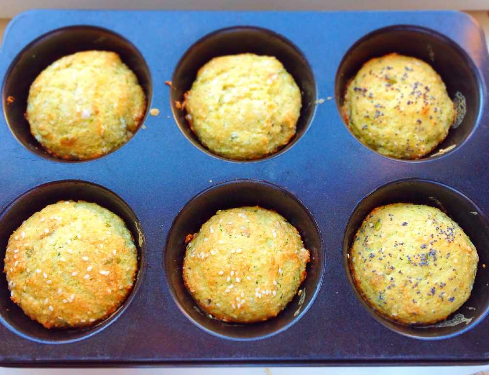 Sex muffins i en svart bakform, med olika toppings som sesamfrön och vallmofrön.